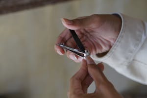 A person using a nail clipper to trim nails with focus on hand and clipper indoors.