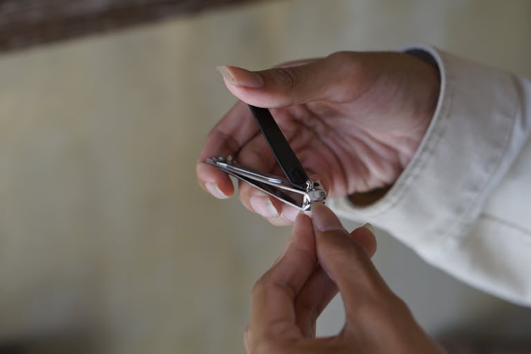 A person using a nail clipper to trim nails with focus on hand and clipper indoors.