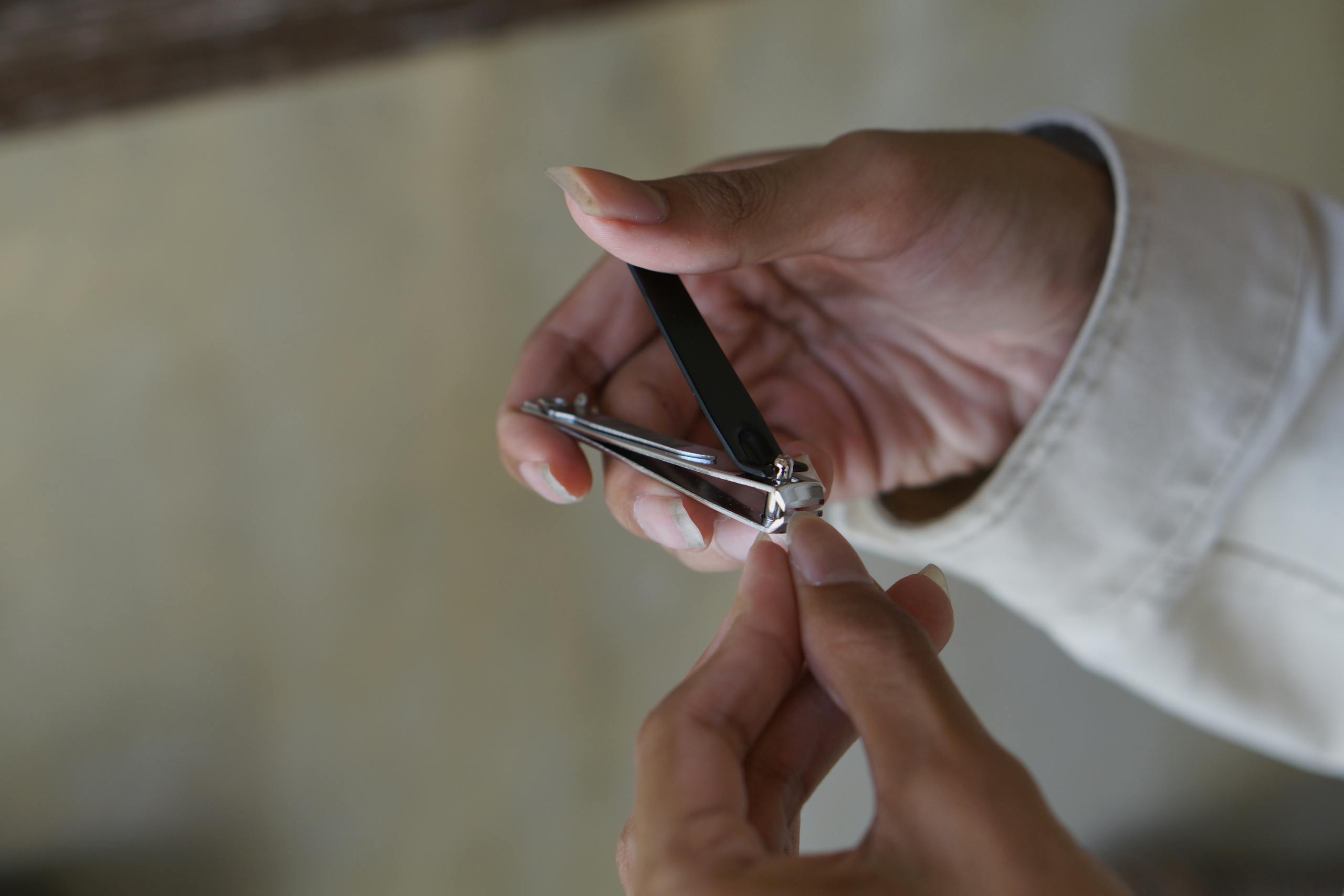 A person using a nail clipper to trim nails with focus on hand and clipper indoors.