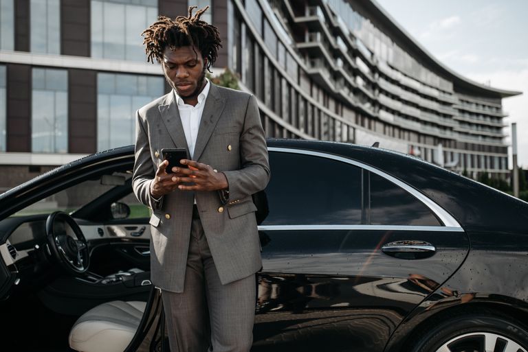 Professional man in a gray suit using his phone next to a luxury car.